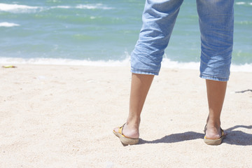 Behind the black of legs woman wearing jeans on beautiful sandy beach tropical sea.