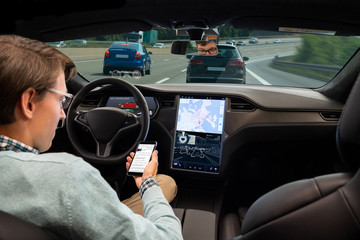 A man reads news online in a smartphone while his car is driven by an autopilot. Self driving...