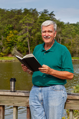 Smiling Senior Man Holding a Book Outdoors and Looking at Camera