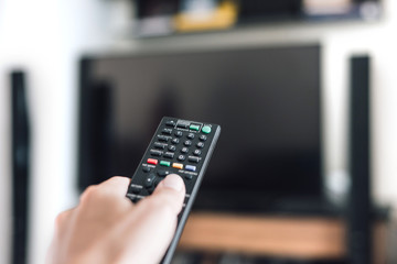 Hand holding remote control with television background in a living room.