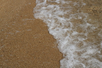     Soft wave of turquoise sea water on the sandy beach. Close-up and directly above photographed 