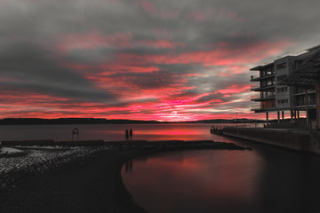 Norwegian sunset taken from the Astrup Fearnley museum in Oslo, the red colors of the sun go out behind clouds behind the sea, while the shadows of people playing on the beach are in motion