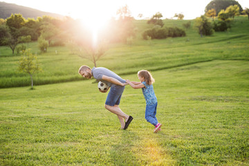 Father with a small daughter playing with a ball in spring nature at sunset.