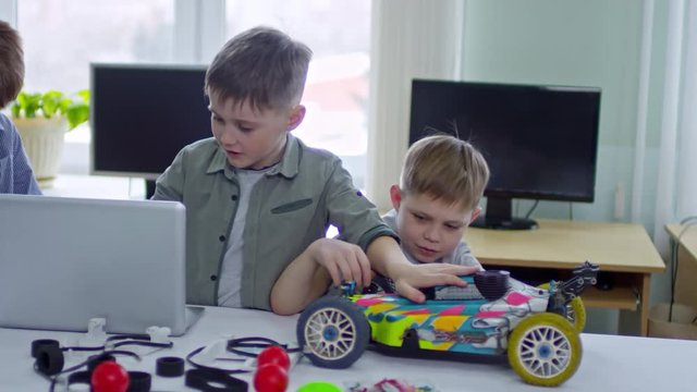 Group of boys of elementary school age using laptop computer, car model and toy details during engineering lesson at school