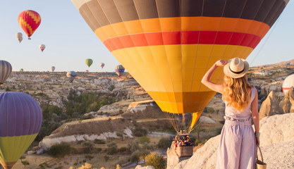 Hipster Traveler with backpack and outspread hands. Enjoying the view of the hot air balloons - obrazy, fototapety, plakaty