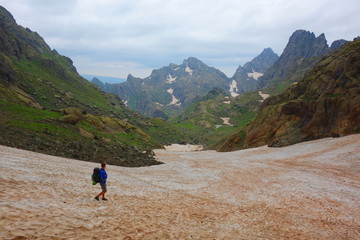 Fototapeta premium Hiking trail with a young man on a snowy Tobavarchkhili mountain pass in Caucasus mountains in Georgia on a hike to Silver Lakes