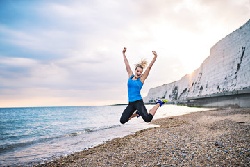 Young sporty woman runner in blue sportswear jumping on the beach outside.