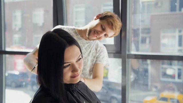 Male hairdresser smiling and talking with a customer while making a new haircut to beutiful young brunette woman