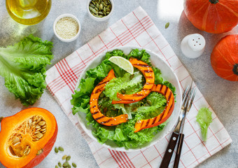 Delicious light salad of grilled pumpkin slices and lettuce with sesame seeds, lemon juice and olive oil. Healthy diet, vegetarian snack