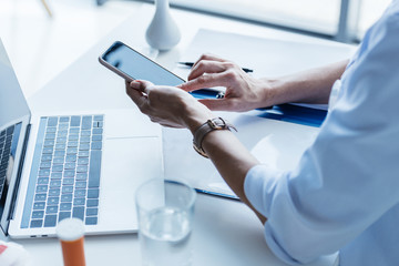 Obraz premium partial view of female doctor using smartphone at table with laptop in office