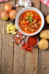 View from above of potato and sausage goulash, pepper, onion and garlic on wooden table vertical photo