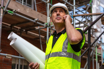 Male Builder Foreman Architect on Building Site Using Phone and Plans