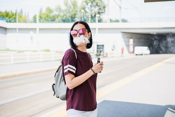 Fototapeta premium Vaping. Young beautiful woman smoking e-cigarette with smoke outdoors. Vapor concept.
