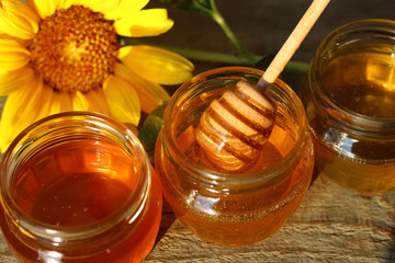 Honey in a glass jar with flowers on the wooden floor.
