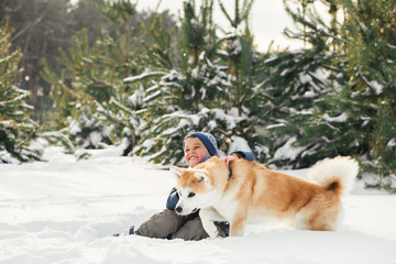 Little child and mom plays with funny Akita-inu dog in a winter park. Christmas happy family,mother and son walking with dog lying on snow in winter day. Drinking hot coffee or tea on snowy winter