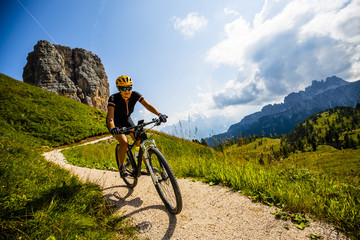 Fototapeta na wymiar Woman cycling in Cortina d'Ampezzo, stunning Cinque Torri and Tofana in background. Riding MTB trail. South Tyrol province of Italy, Dolomites.