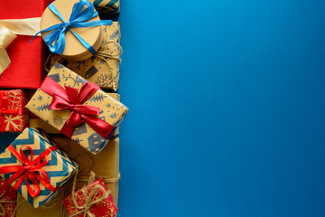 Top view on Christmas gifts wrapped in gift paper decorated with ribbon on blue paper background....