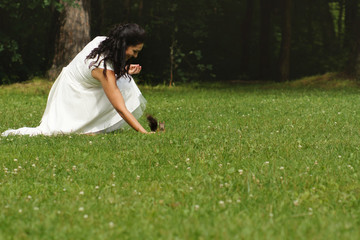 Beautiful brunette in white dress squatting in park and feeding red squirrel