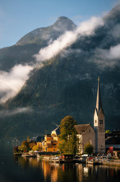 Scenic view of famous Hallstatt lakeside town reflecting on Hallstattersee lake in the Austrian Alps in morning light in autumn with bushes and flowers on the foreground, Salzkammergut region, Austria