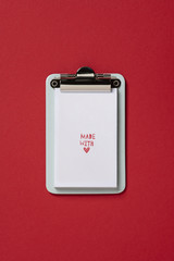Clipboard made with love, on red background. Flat lay, top view trendy for banner