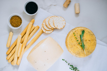 Assorted сachotta cheese with black cumin, fenugreek and herbs with jam, baguette, bread sticks and crackers on marble background