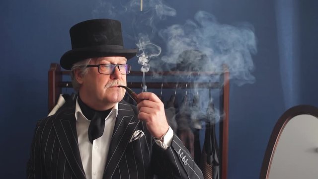 Portrait of posh chic virile millionaire or rich mature man visiting a luxury fashion boutique for buing new exclusive suit, smoking tobacco pipe