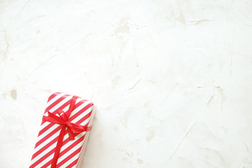 Obraz premium Christmas and new year present wrapped in festive colorful red and white stripe pattern paper. Single holiday gift box on white concrete texture table. Close up, background, copy space, top view.