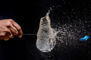 Bursting of a blue balloon filled with water with a long pin on black background. 