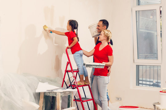 Happy family mother father and child daughter are doing repairs paint wall at home
