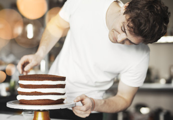 Close up of young man decorating chocolate cake by butter cream.