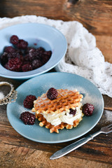 Fototapeta na wymiar Round waffles with fresh blackberries and whipped cream, on natural wooden background in rustic style