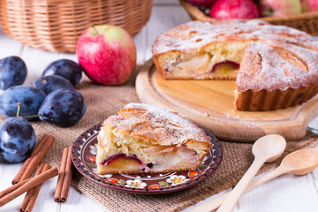 Plum and apple pie, cut on wooden background