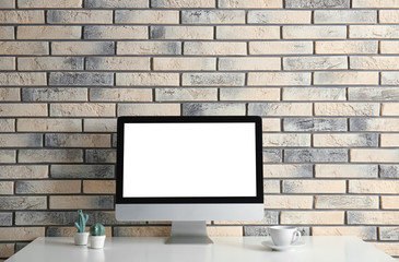 Fototapeta premium Modern computer monitor on table against brick wall. Mock up with space for text
