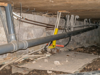 Suspended foundation under old house is often called crawl. Pipes for drain, sewer, water and electricity.