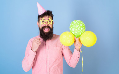 Man with beard on happy face hold air balloons, light blue background. Guy in party hat with air...