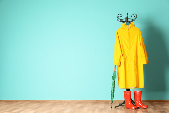 Umbrella, rain coat and boots near color wall with space for design