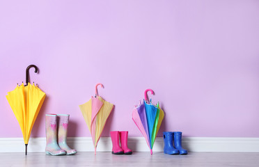 Beautiful umbrellas and gumboots on floor near color wall with space for design