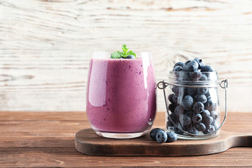 Glass of smoothie and jar with blueberries on wooden table