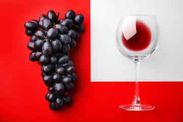 Glass with red wine and fresh ripe juicy grapes on color background, top view