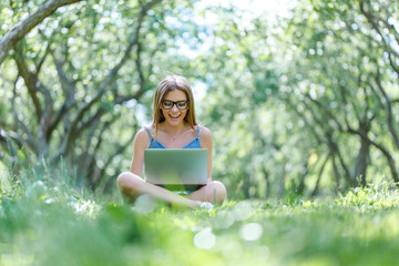 Young woman with notebook in park looking at notebook computer