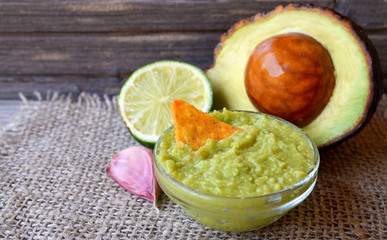 Traditional mexican homemade guacamole sauce in a glass bowl with half of avocado,
lemon and nachos corn chips.Selective focus. 