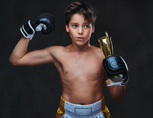 Fototapeta na wymiar Young shirtless boxer champion wearing gloves holds a winner's cup showing muscles.