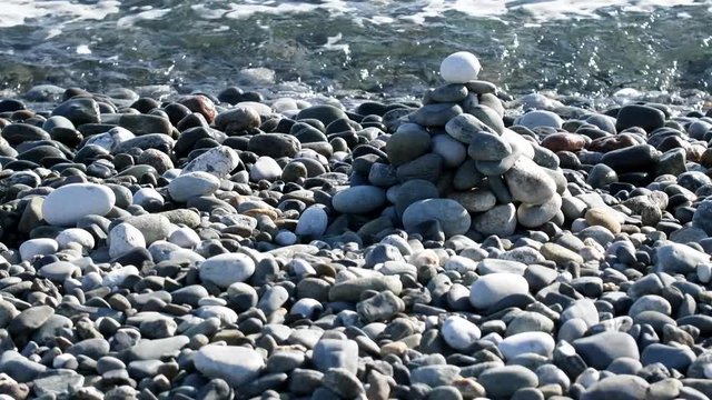 Pebble sea beach and a pyramid of small stones on the edge of the surf as entertainment for vacationers
