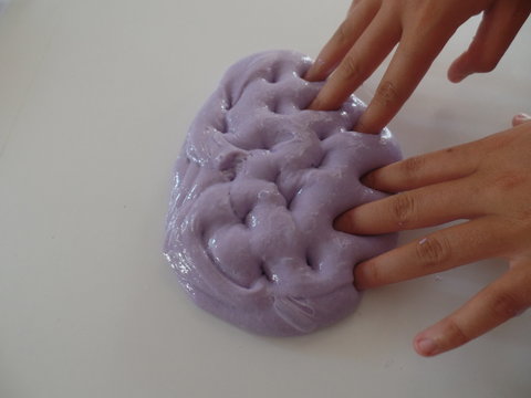 Child's hand poking lilac coloured glossy slime