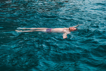Fototapeta na wymiar man swimming on back in blue transparent sea water