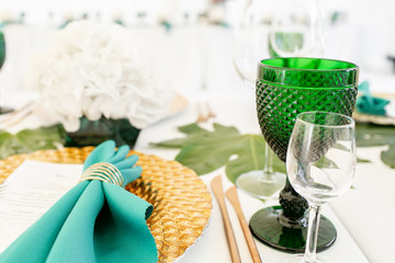 Interior of tent for wedding diner, ready for guests. Served round banquet table outdoor in marquee decorated hydrangea flowers, Golden dishes and green napkins. Catering concept