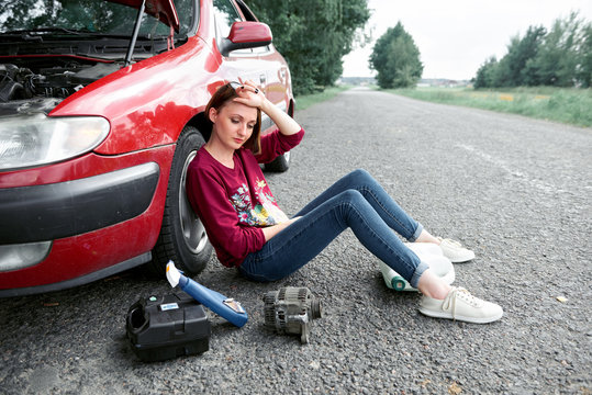 A Young Girl Sitting Near A Broken Car And Looking For Help, Next To Her There Are Bad Parts, Electric Generator, Tools And First Aid Kit