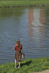 samotna dziewczyna z torebką patrzy w odbicie na wodzie, smutek i zamyślenie w czasach pandemii - obrazy, fototapety, plakaty