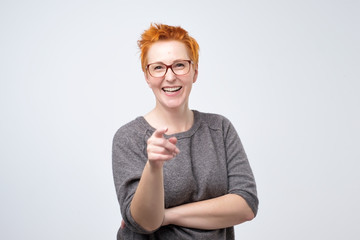 Happy mature fashion woman with red hair posing for the camera while pointing at you. She points to you as the winner
