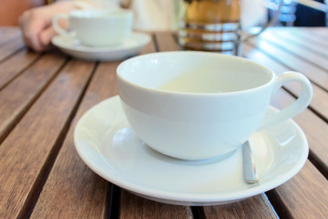 Two teacups and French press on the table, blurred woman behind.